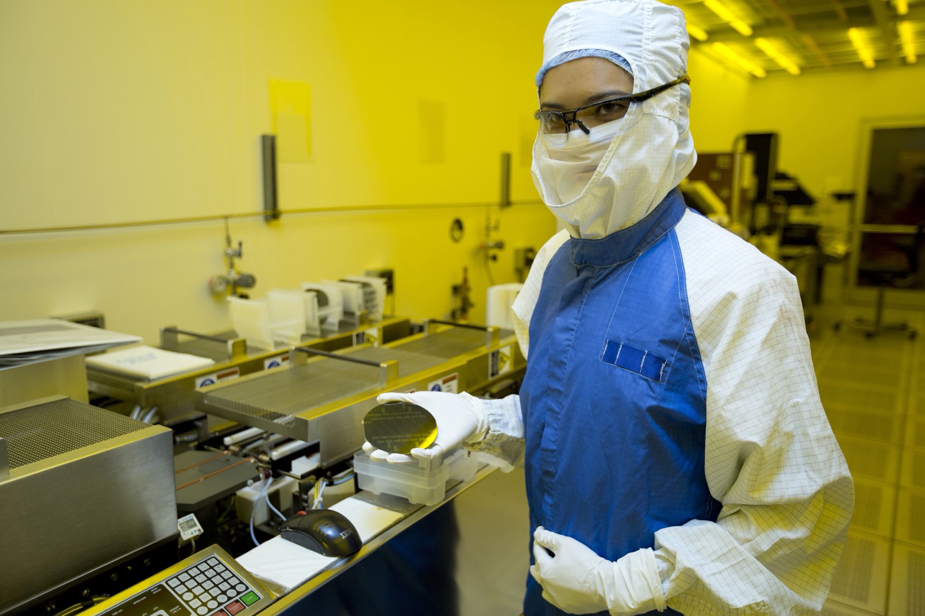 A gowned researcher in a cleanroom holding a semiconductor wafer